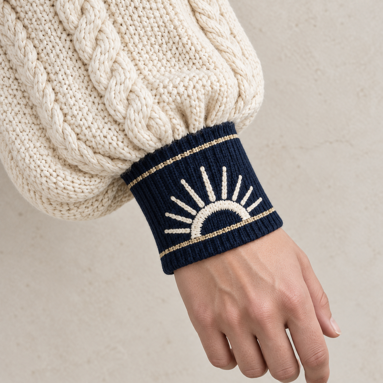 Strickentwurf mit plastischem elfenbeinfarbenem Ärmel, Navy-Manschette und goldfarbenen Garnlinien